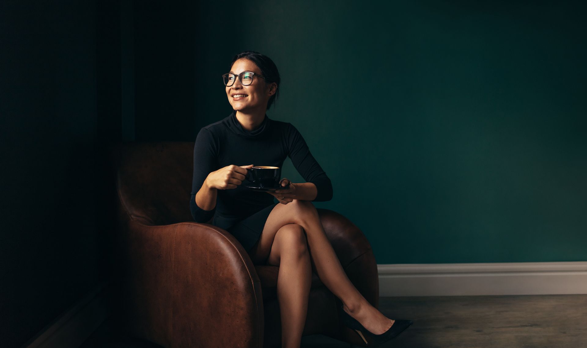 A woman is sitting in a chair with her legs crossed and holding a cup of coffee.