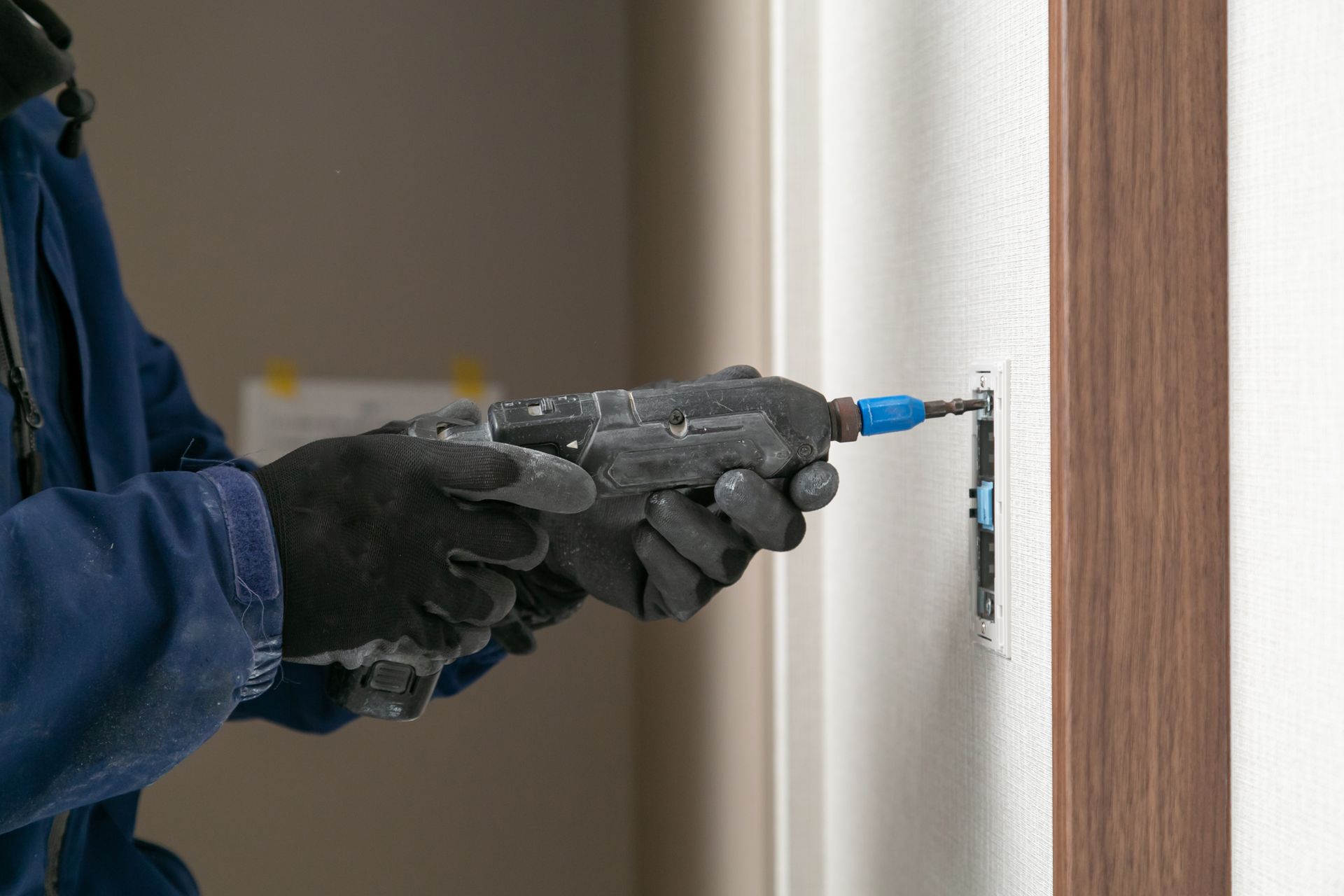 Person using a drill to install a wall anchor beside a wooden trim board.