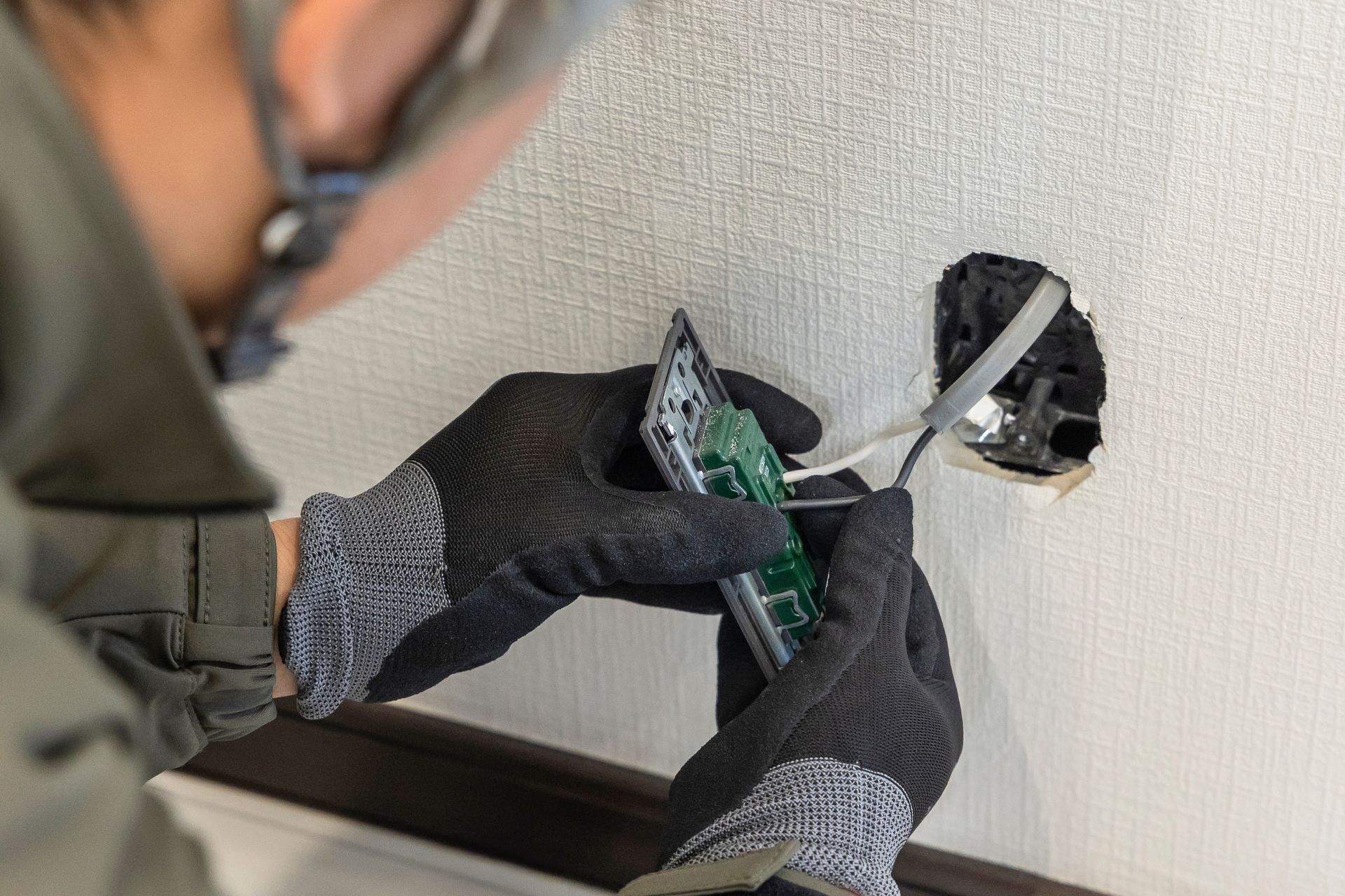 Technician installing a wall outlet with green electrical wires and a screwdriver.
