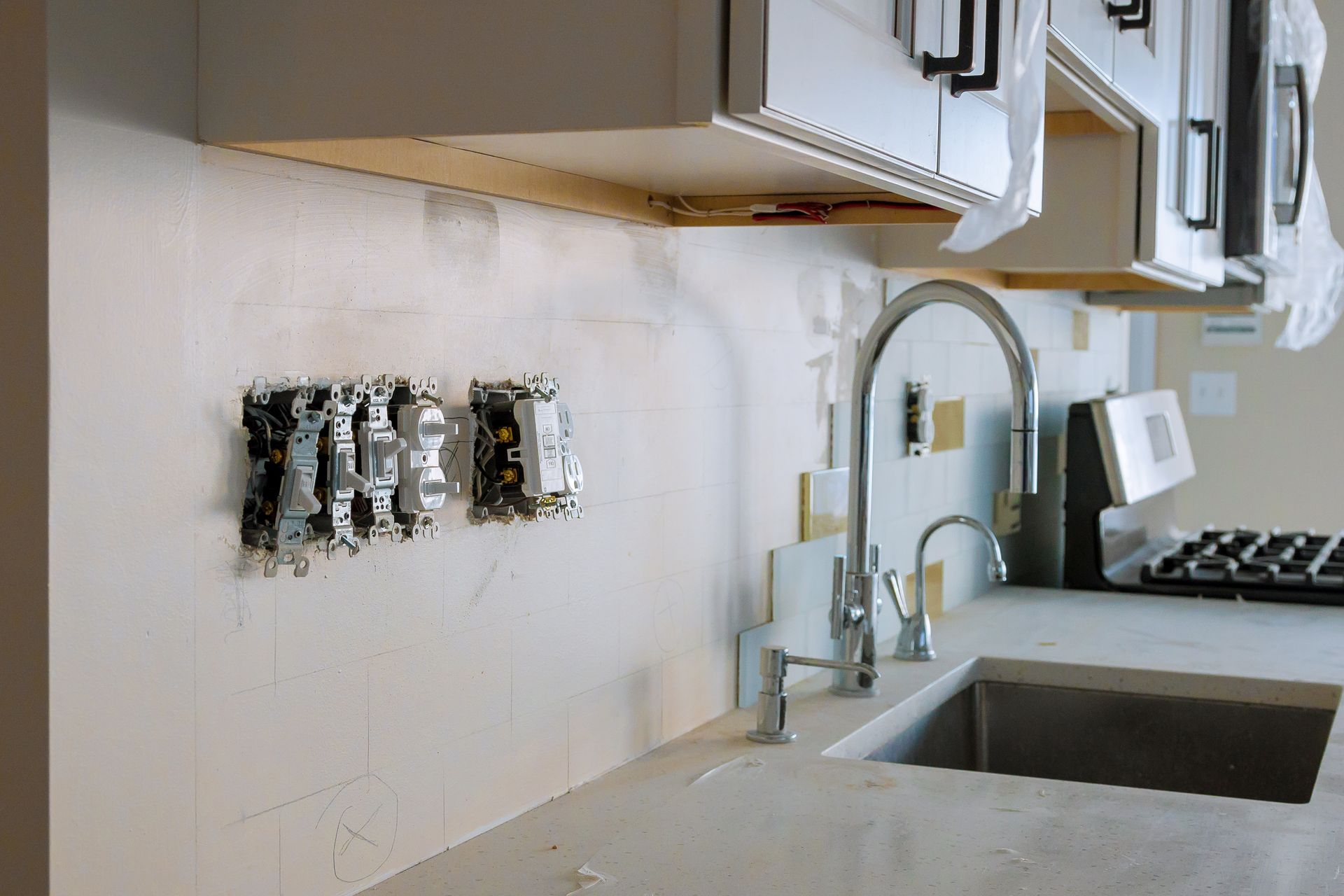 Kitchen wall with exposed electrical outlets above a countertop sink and faucet under white cabinets. Kitchen wall with exposed electrical outlets above a countertop sink and faucet under white cabinets.