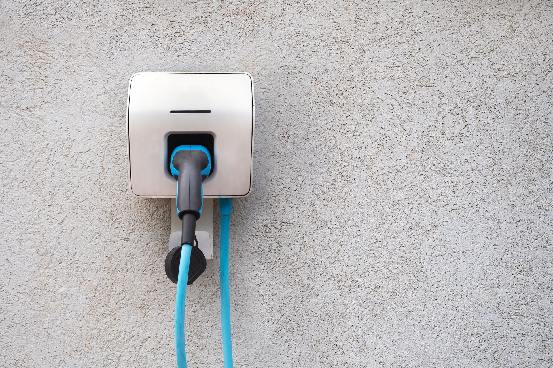Wall outlet with a black plug and blue cable on a textured gray wall.