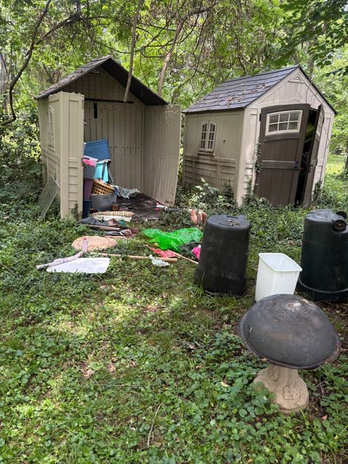 Two small sheds in a messy backyard with scattered debris and containers on the grass.