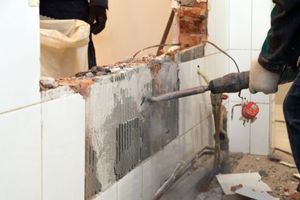 Workers using a jackhammer to break a tiled wall during demolition work