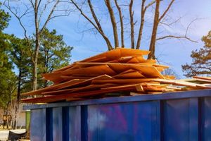 Stacked wooden boards on a blue dumpster outdoors under bare trees