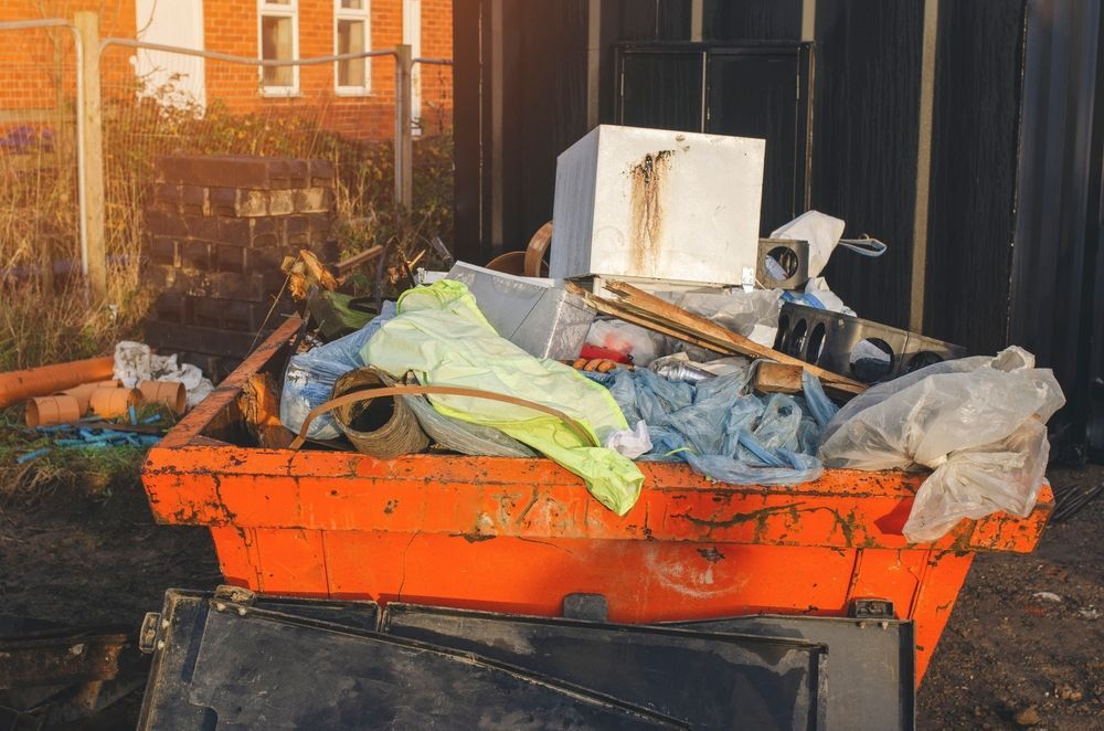 Orange dumpster piled with trash and debris beside a building