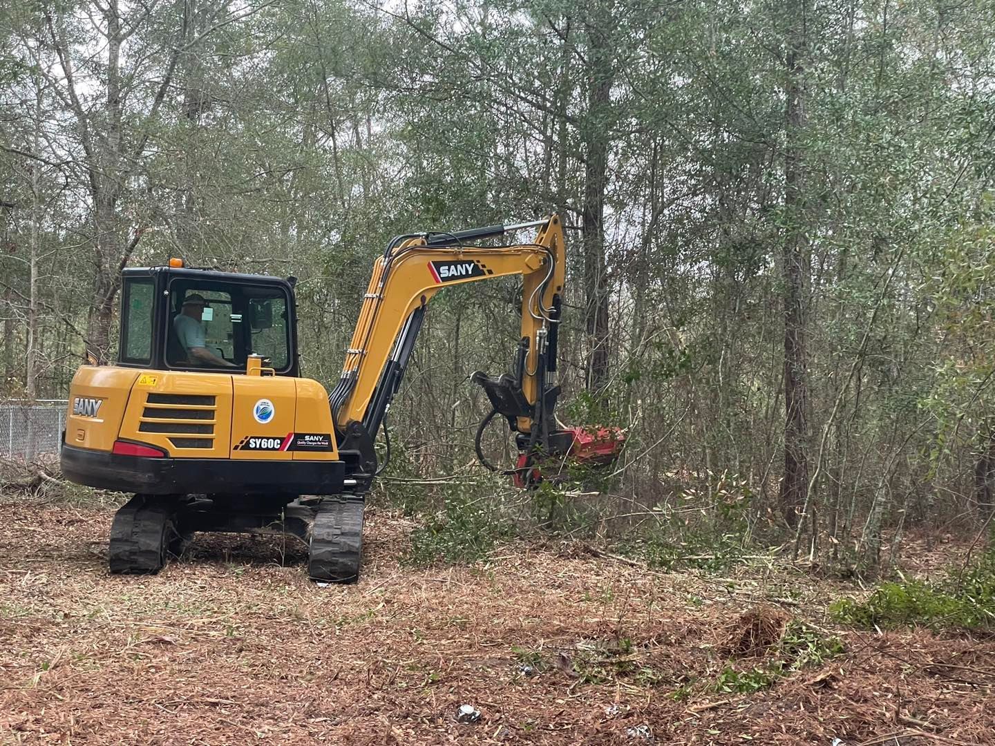 A yellow excavator is cutting down trees in a forest.