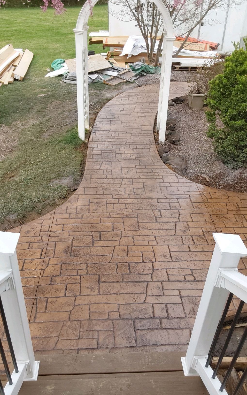 Brick walkway leading to a backyard patio with white railings and a garden arch