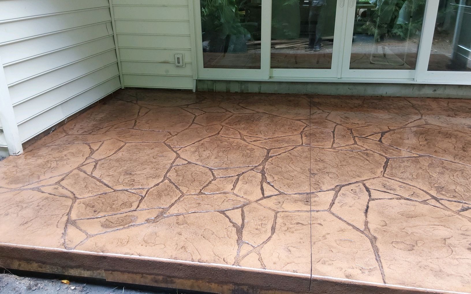 Cracked stamped concrete patio beside a house with sliding glass doors and white siding