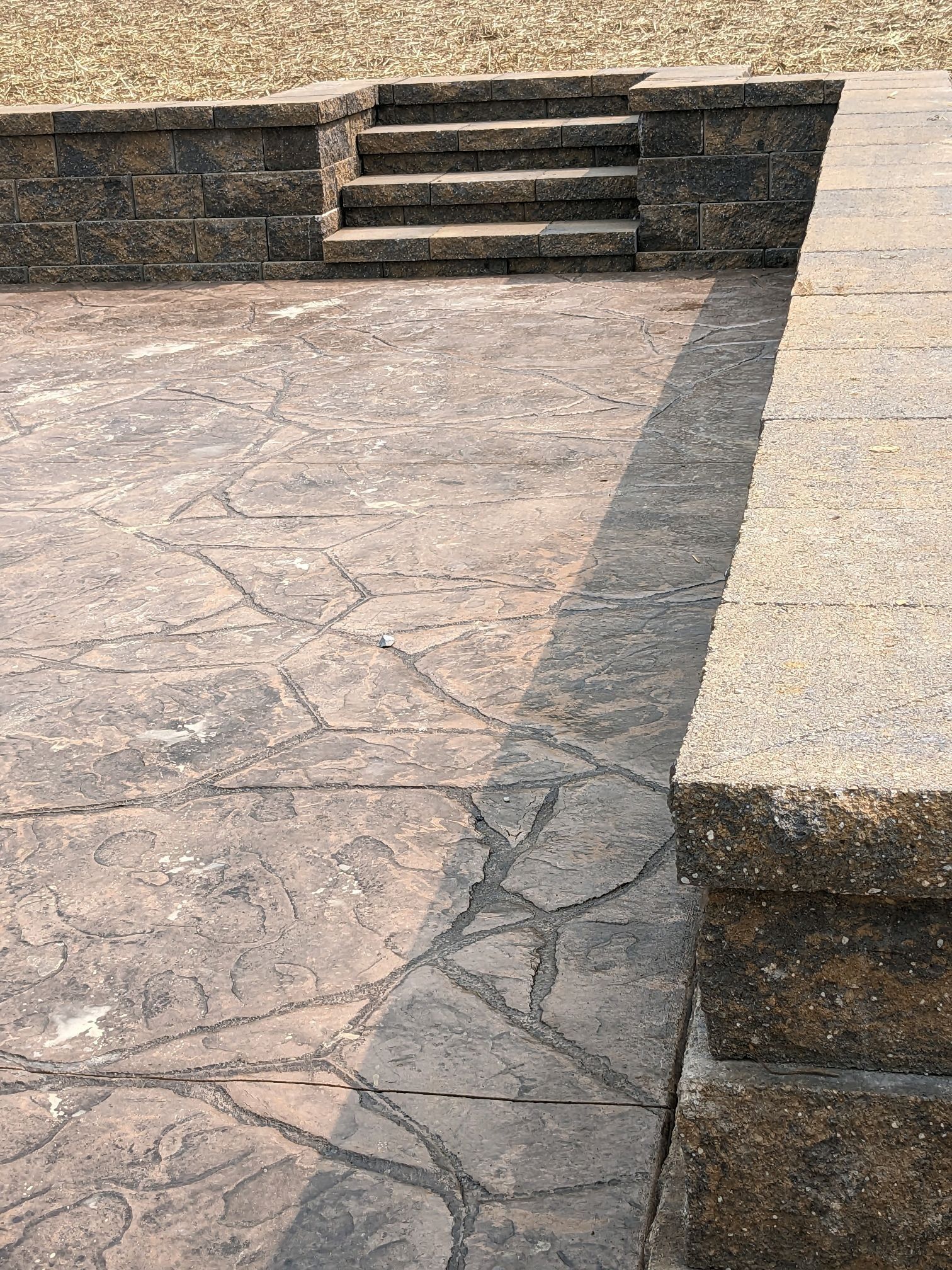 Stone steps leading up from a sunlit paved courtyard with low stone walls.
