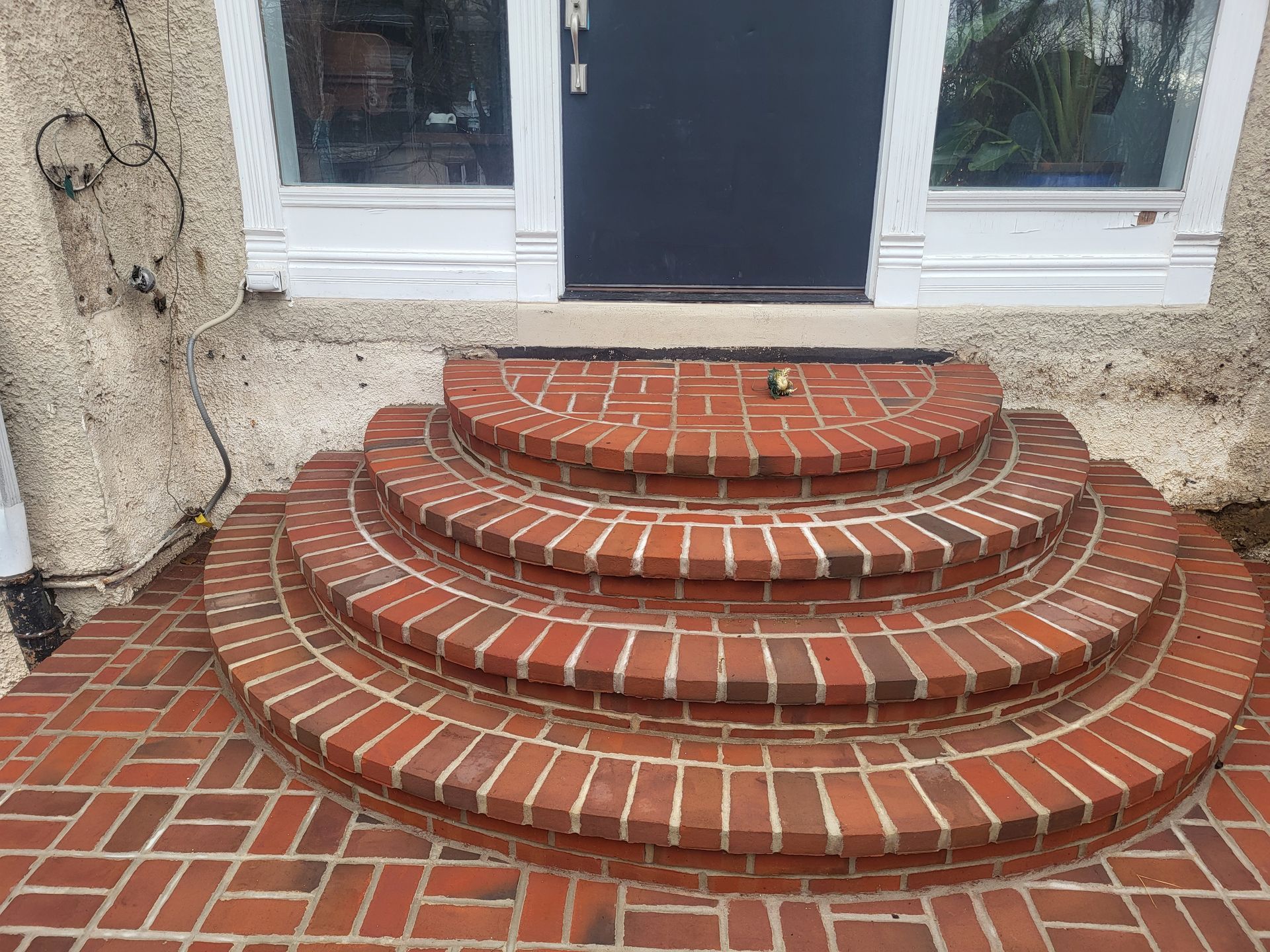 Brick semicircular front steps leading to a white door and windows on a house porch