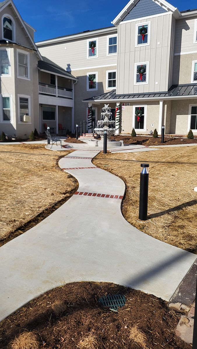 Apartment courtyard with a winding concrete path, mulch beds, and tan buildings under a bright blue sky