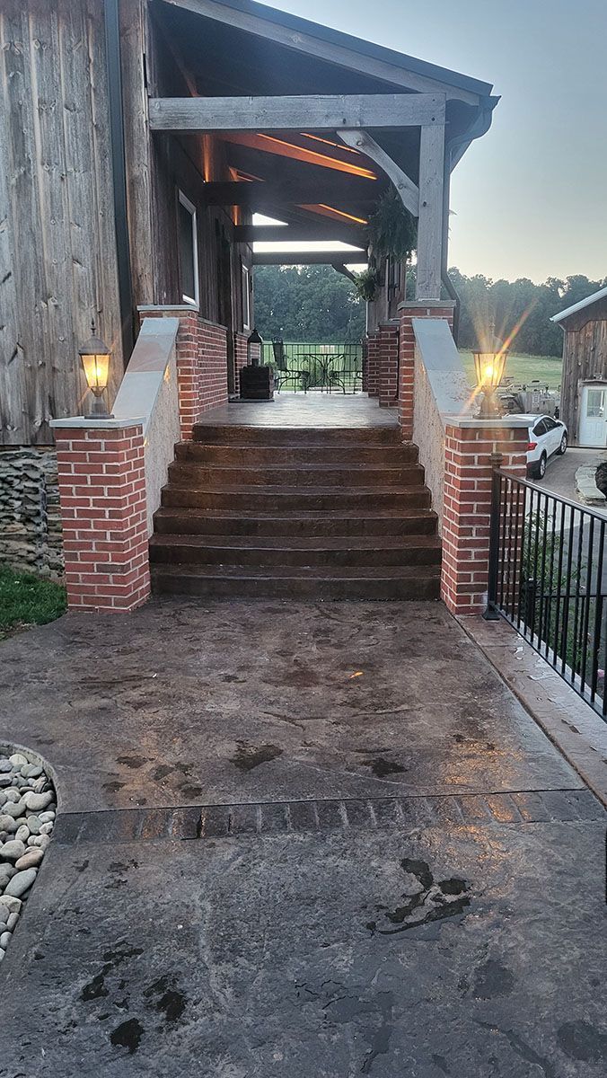 Covered stone walkway with brick steps and railings leading to a lit front entrance at dusk