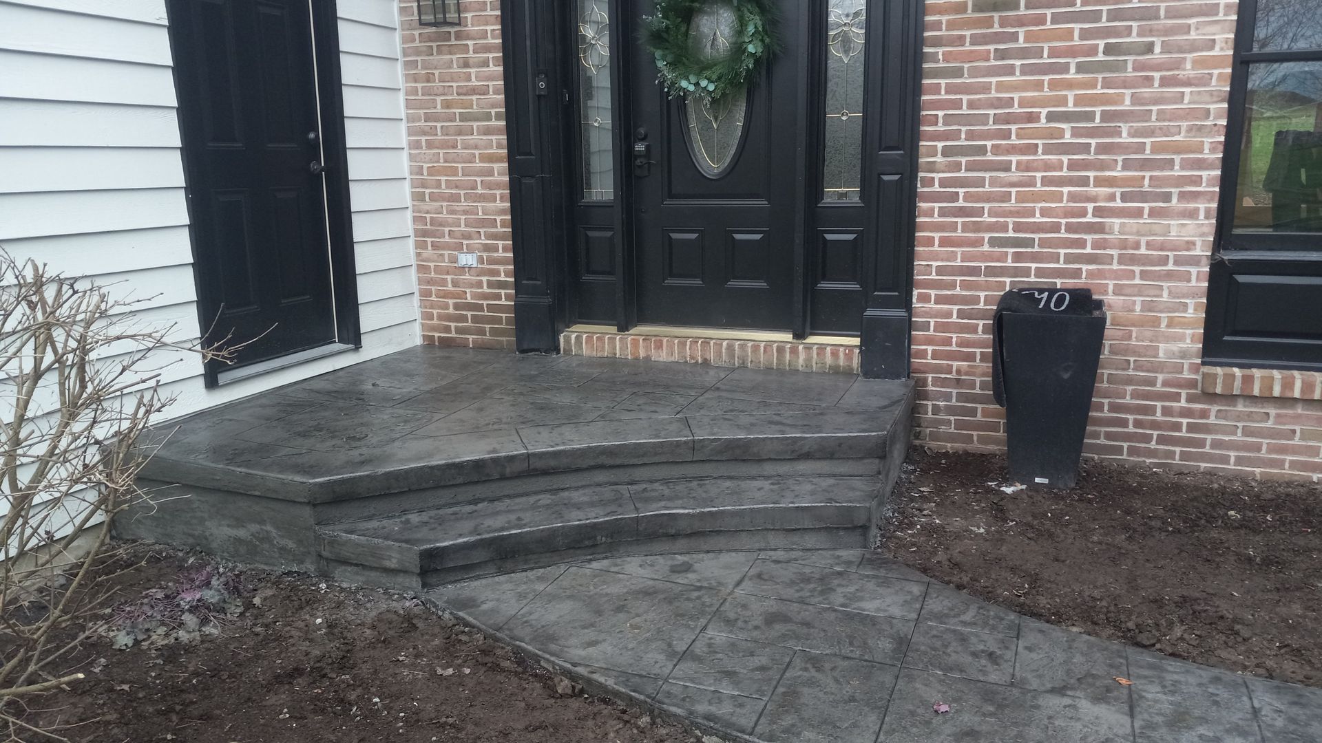 Front porch with brick steps, black double doors, and a wreath