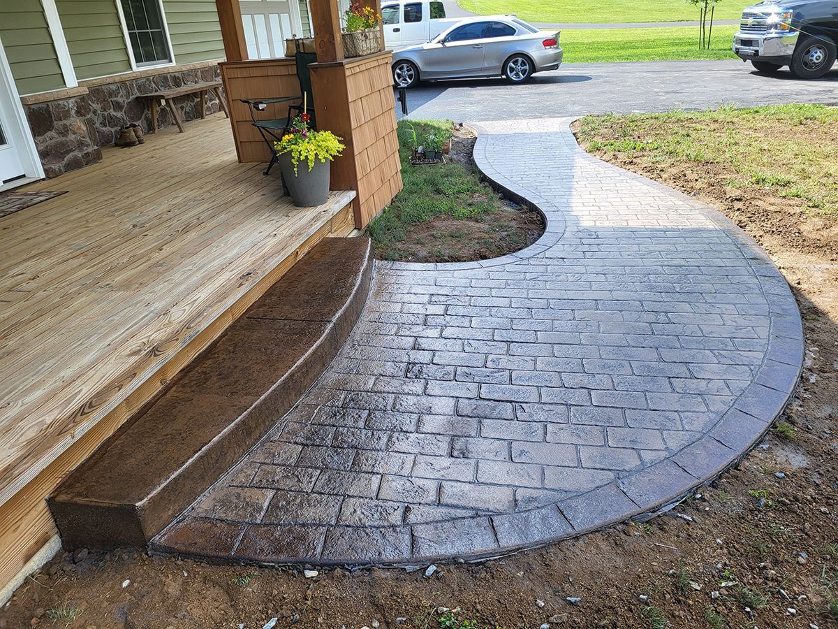 Brick-paver curved walkway leading to a front porch, with a potted plant and parked cars in the background