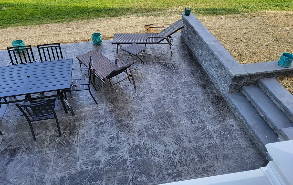 Outdoor patio with metal table and chairs beside concrete steps and a grassy yard.