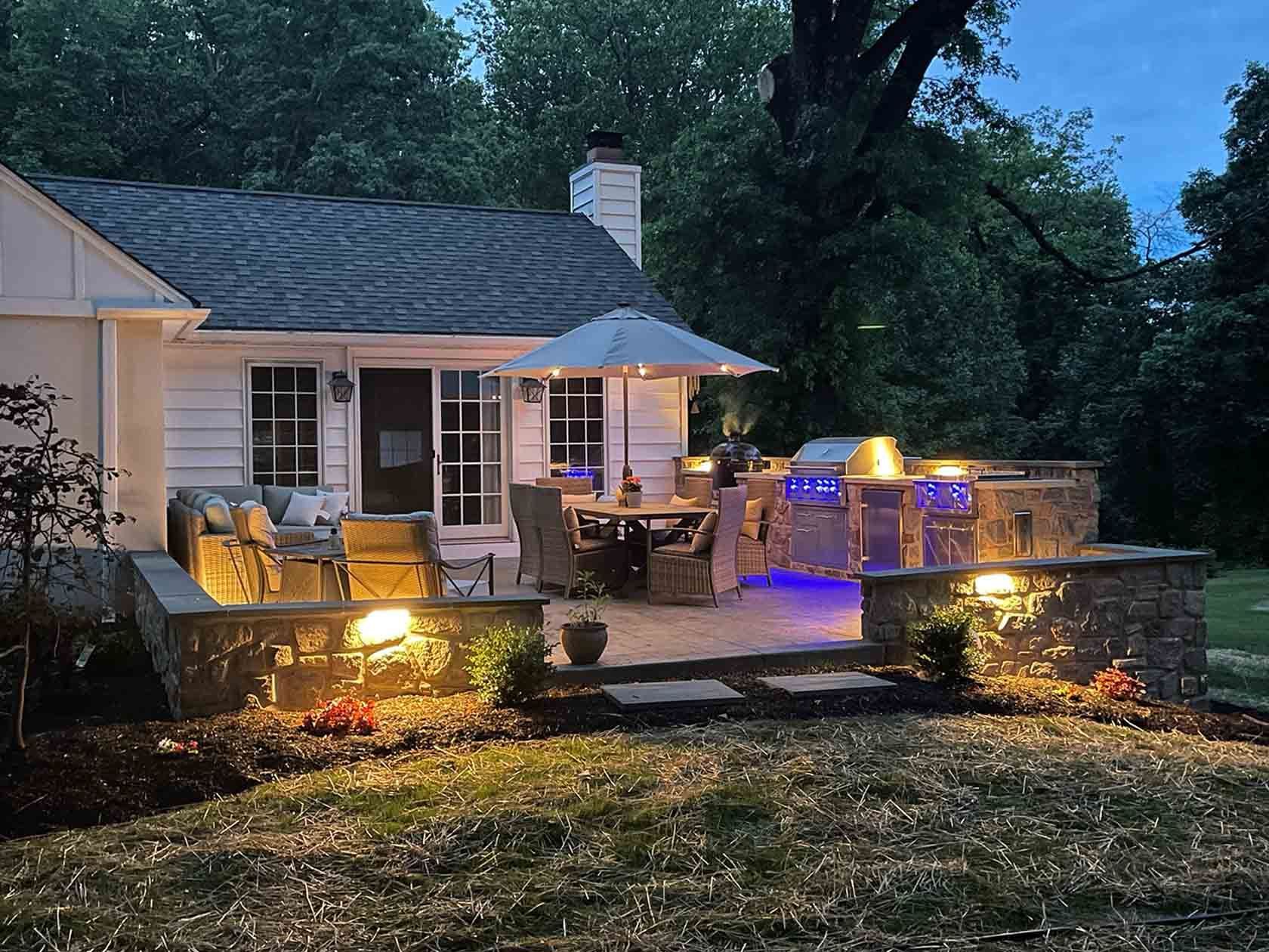 Backyard deck at dusk with glowing outdoor lights beside a house and lawn