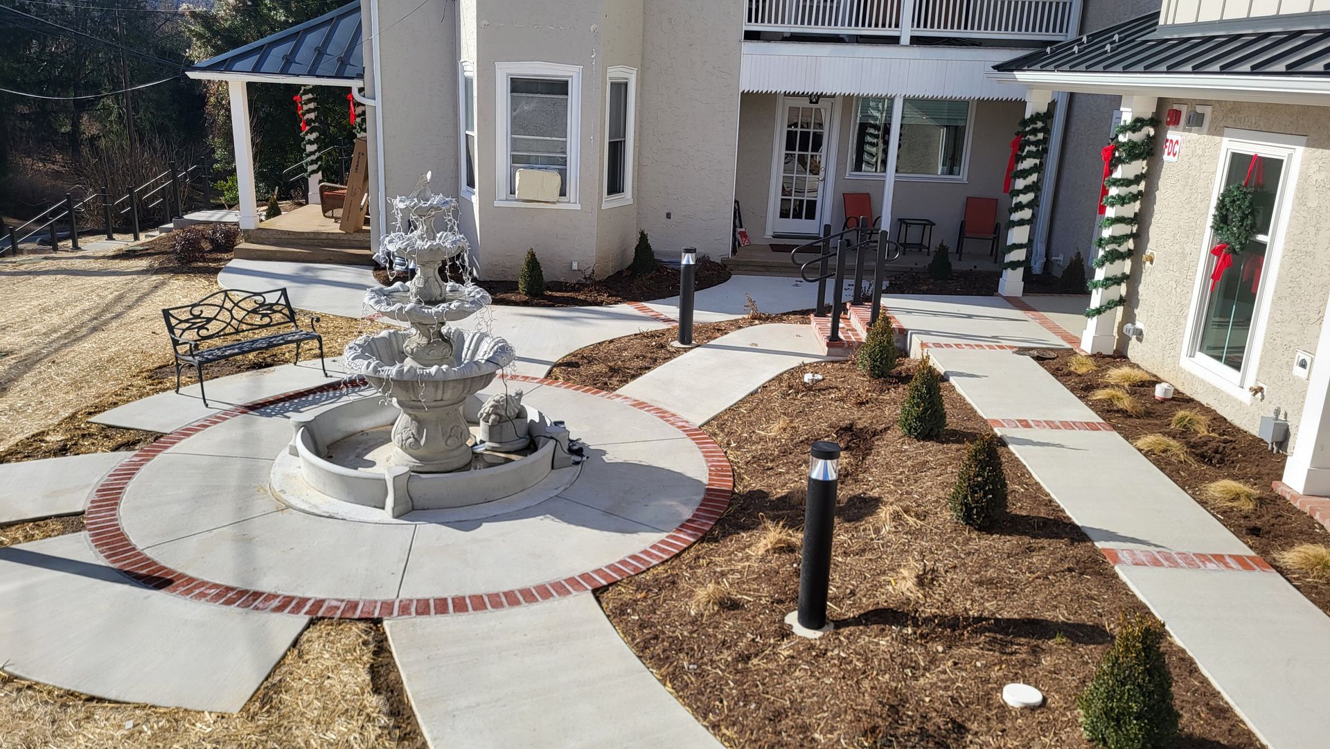 Courtyard with a small fountain, curved stone paths, and landscaped flower beds beside a white building