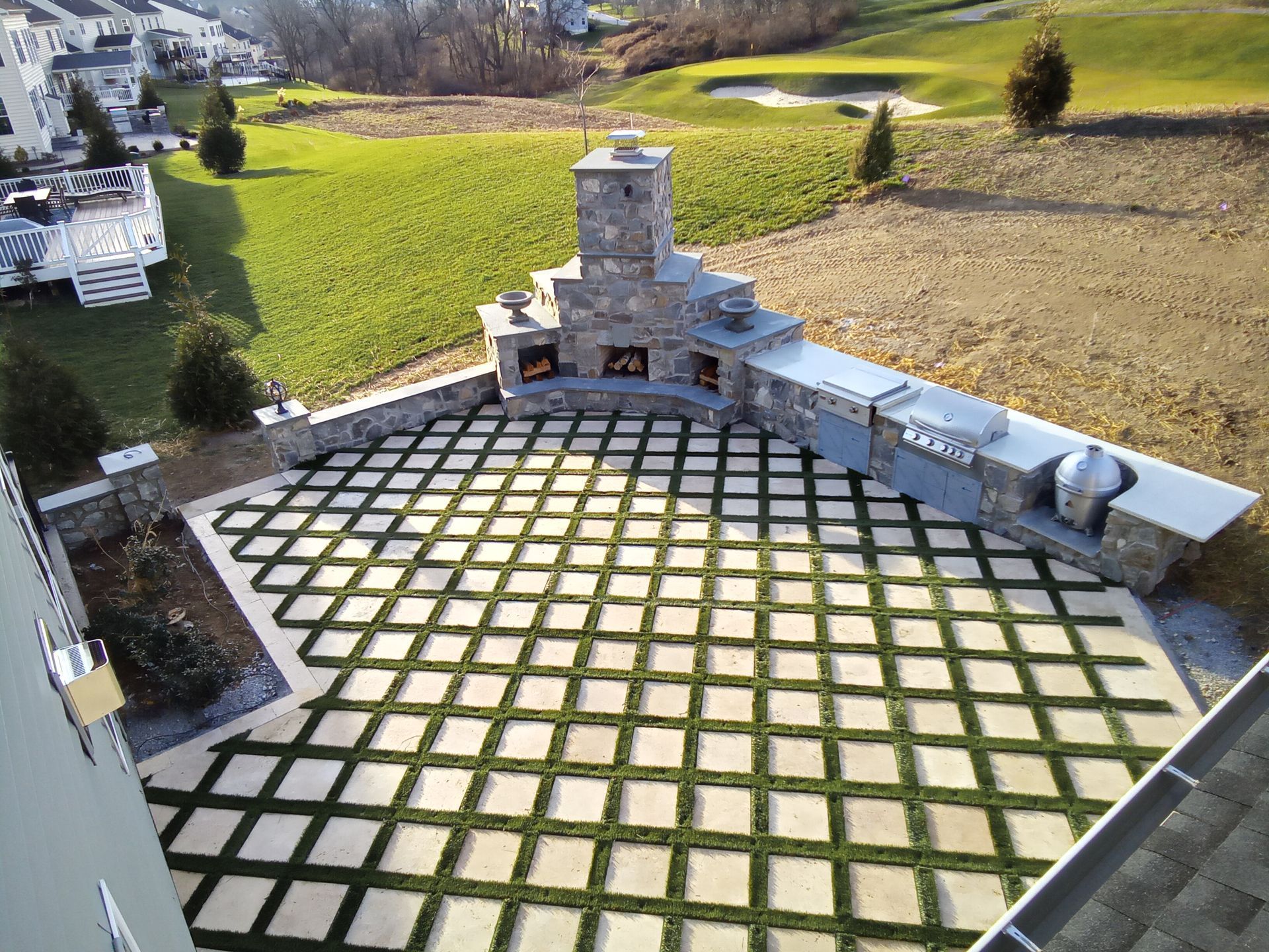 Stone outdoor amphitheater with a checkerboard lawn and surrounding fields under bright sunlight