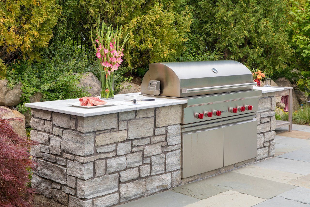 Outdoor stone patio kitchen with stainless steel grill, countertop, and flower vase