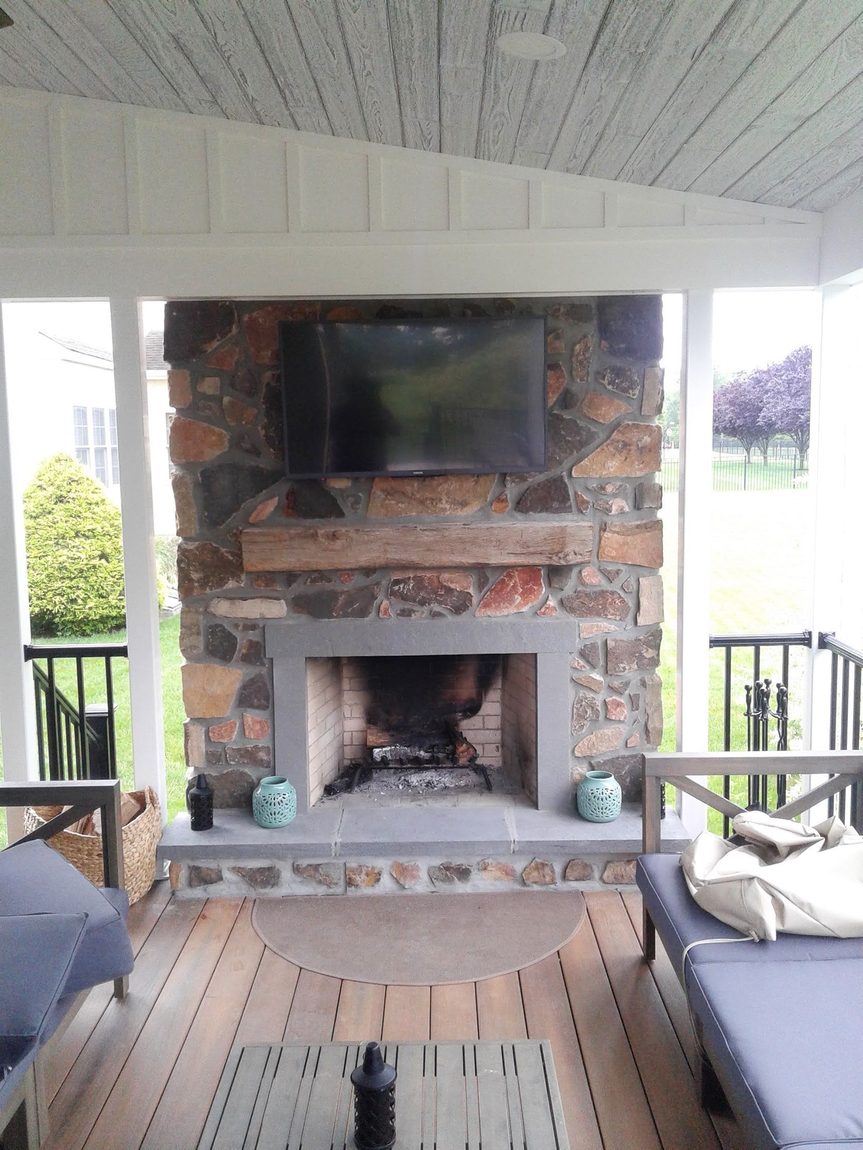 Outdoor covered patio with a stone fireplace, TV, and wicker seating area