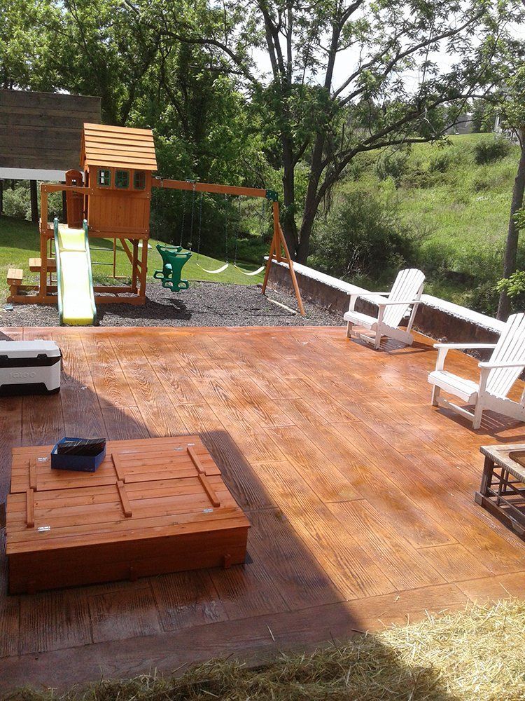 Backyard deck with wooden playset, slide, chairs, and a hot tub beside trees and grass.