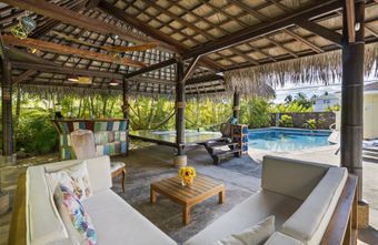 Open-air patio with wicker seating, coffee table, and pool view under a thatched roof