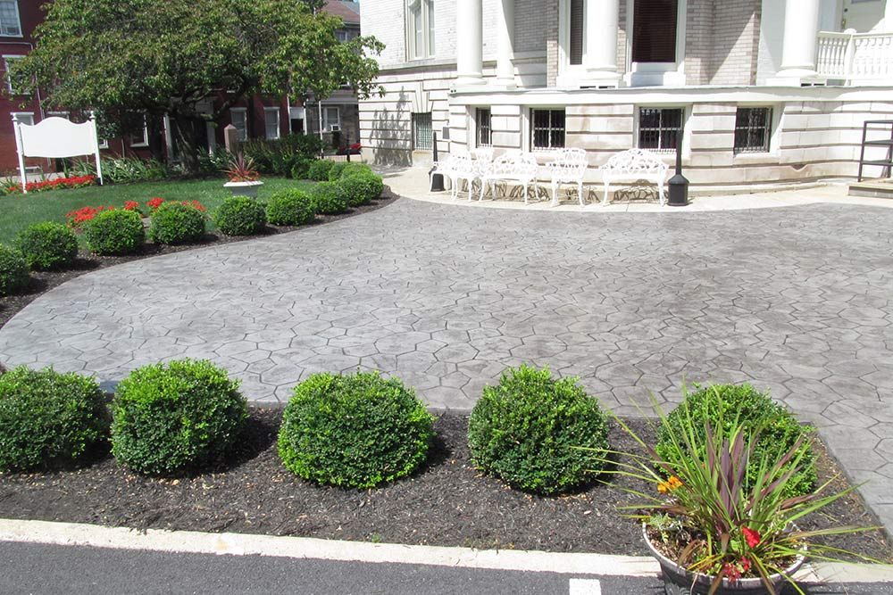 Landscaped courtyard with gravel path, green shrubs, flower beds, and a stone building in the background