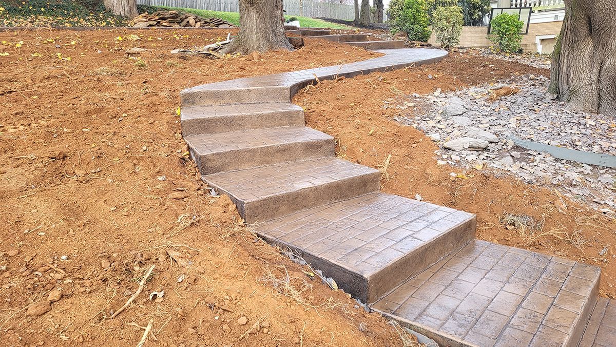 Curved concrete steps through a mulched garden beside trees and a gravel path