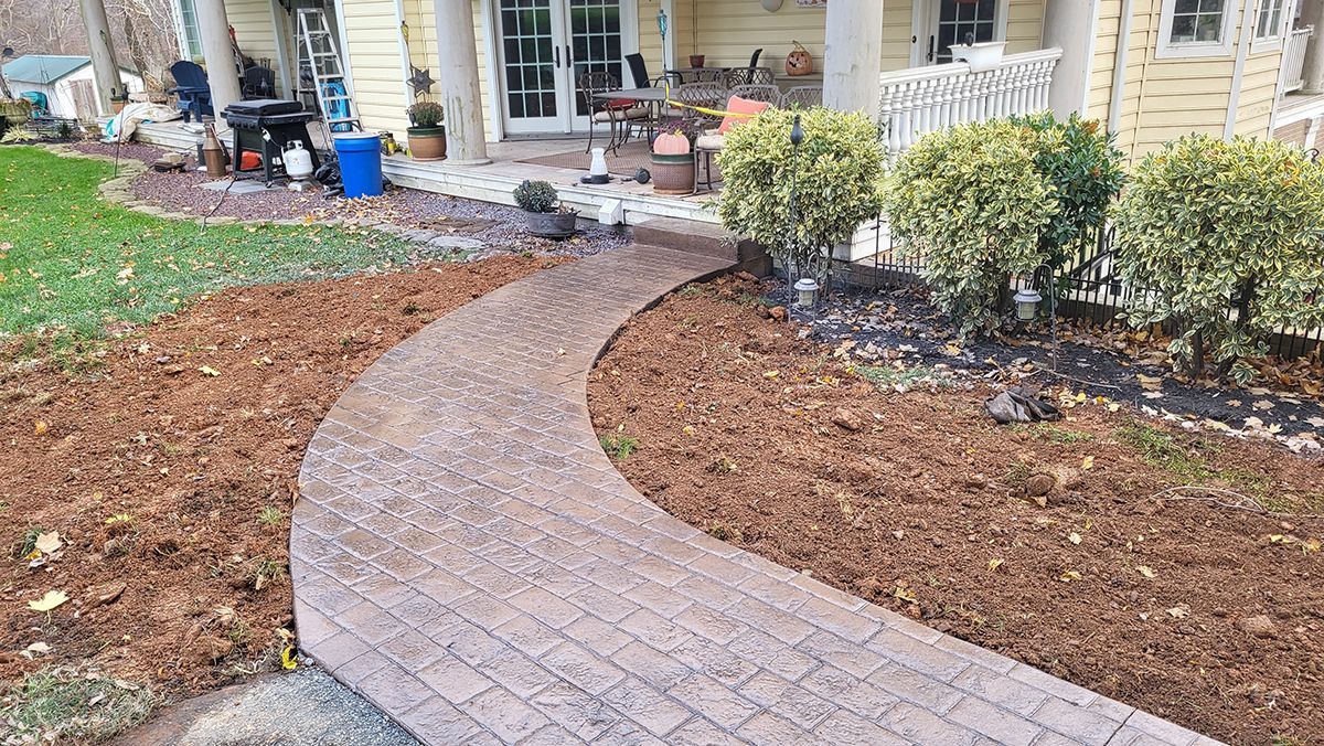 Curved brick walkway leading to a house entrance, bordered by mulch and shrubs.