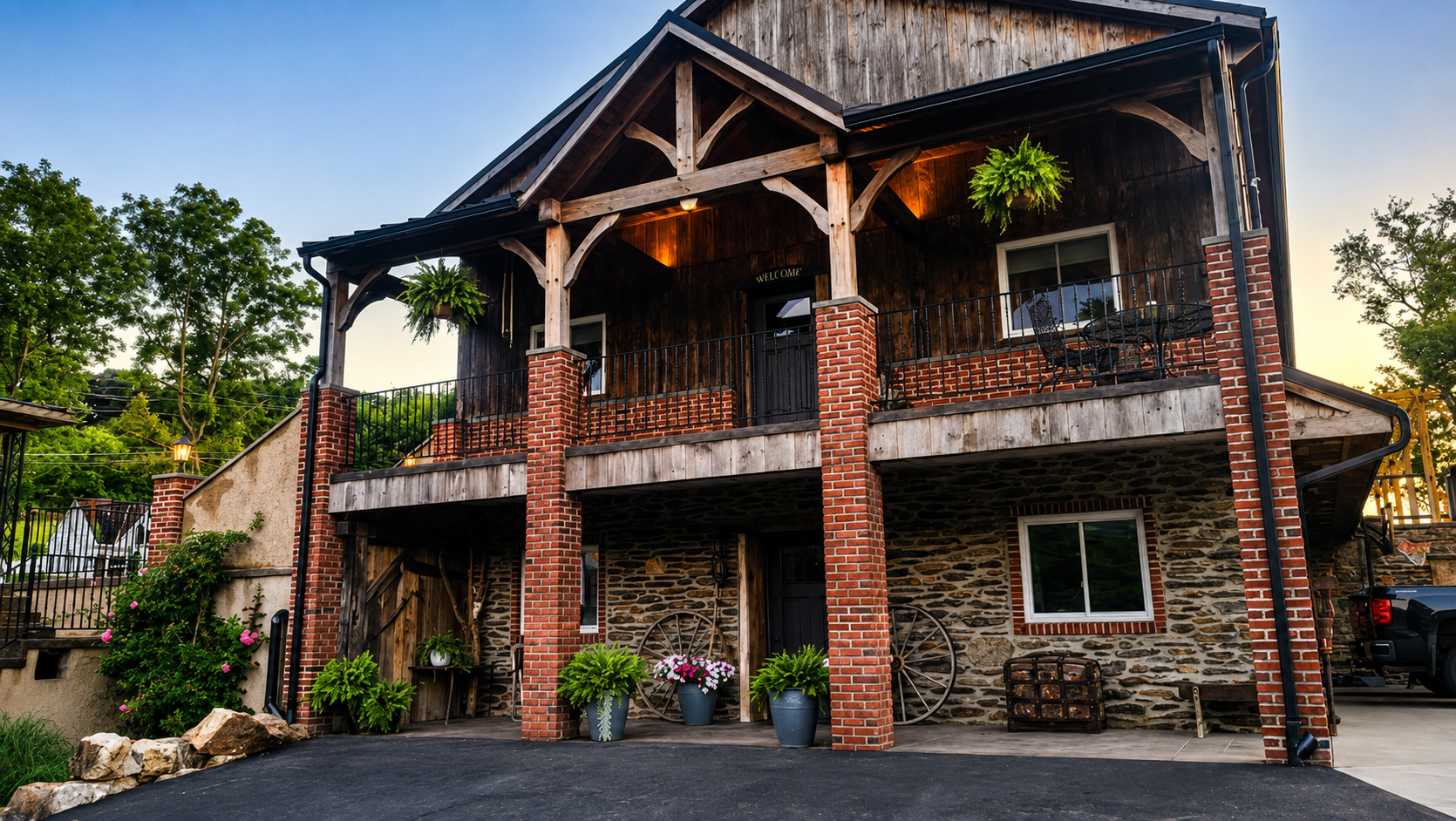 Rustic two-story stone and wood house with a covered porch, brick columns, and potted flowers