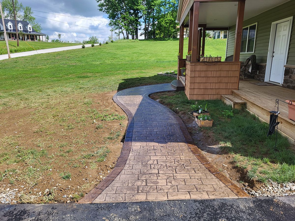 Brick path leading through a grassy yard beside a house and porch under sunny skies
