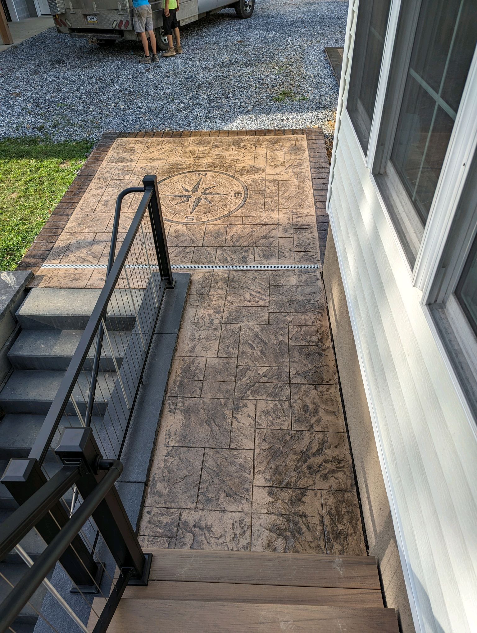 Steep outdoor concrete steps with black railings beside a white house, leading to a gravel driveway.