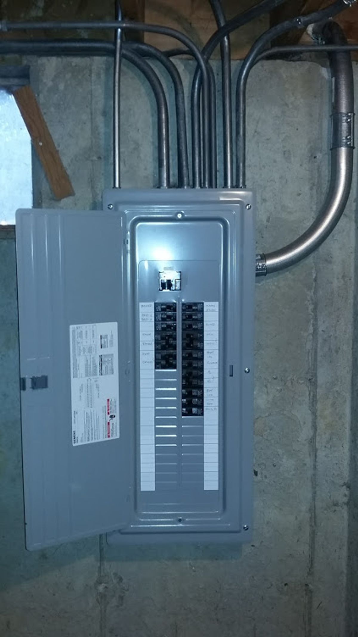 A gray electrical box is hanging on a concrete wall.