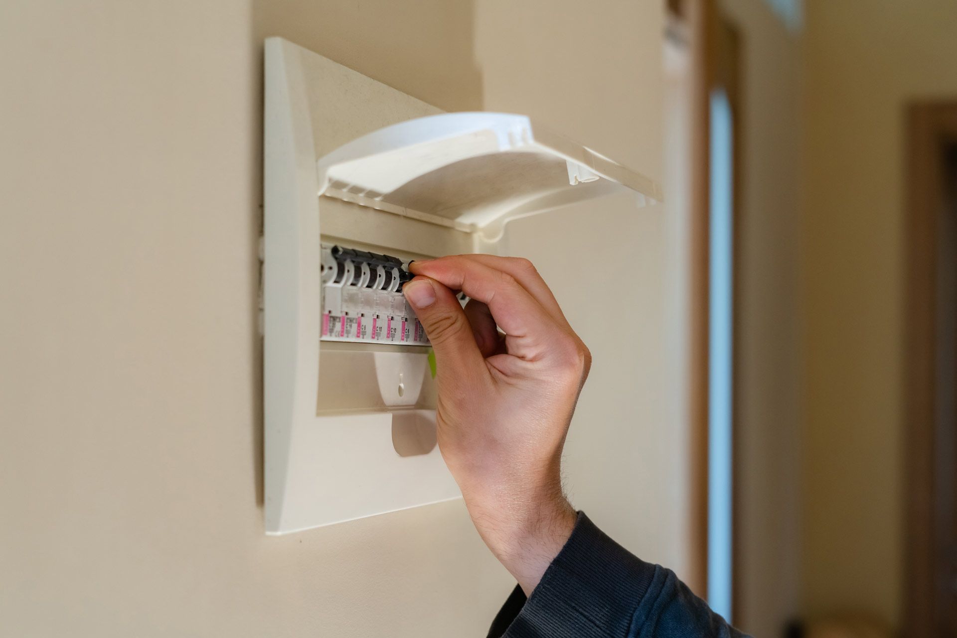 A person is opening a electrical box on a wall.