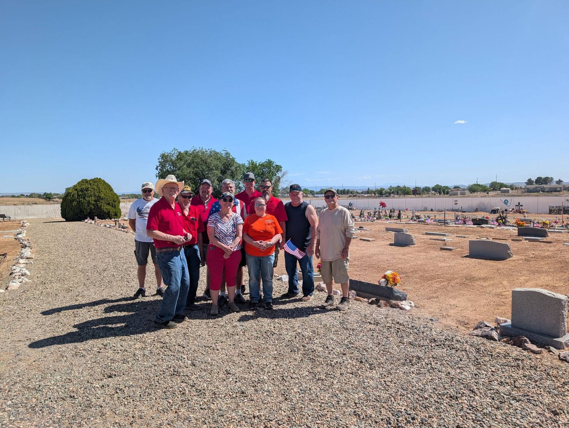 Group of people standing on a gravel path in a sunny desert landscape with sparse shrubs and cacti.
