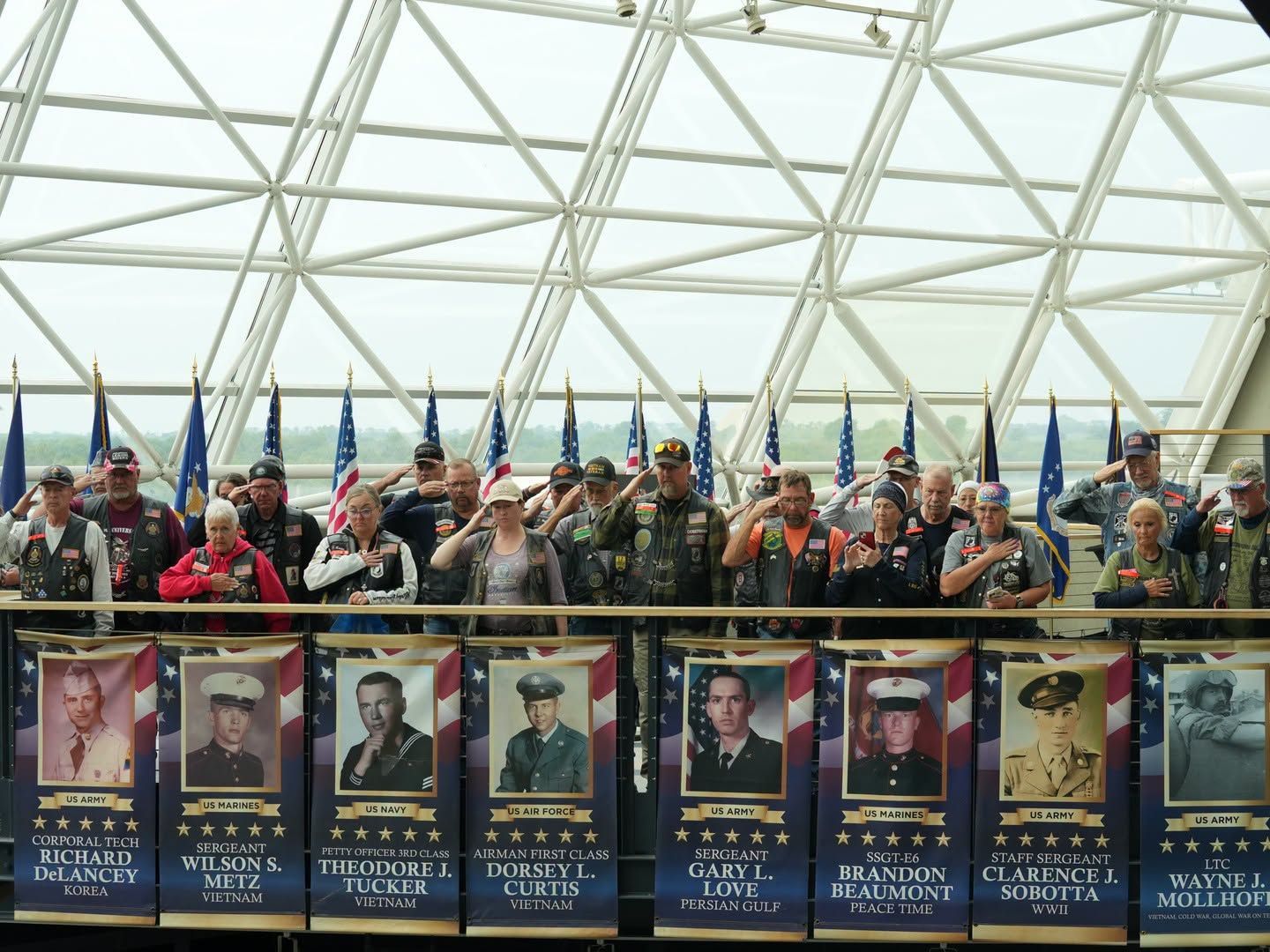 People holding flags and military portraits in a glass atrium memorial display