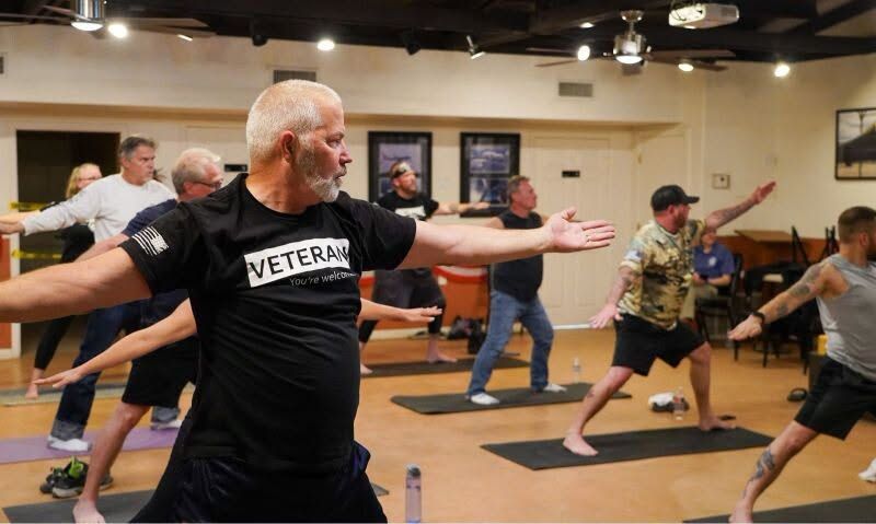 Veterans in a yoga class holding a warrior pose in a studio with mats and wall art