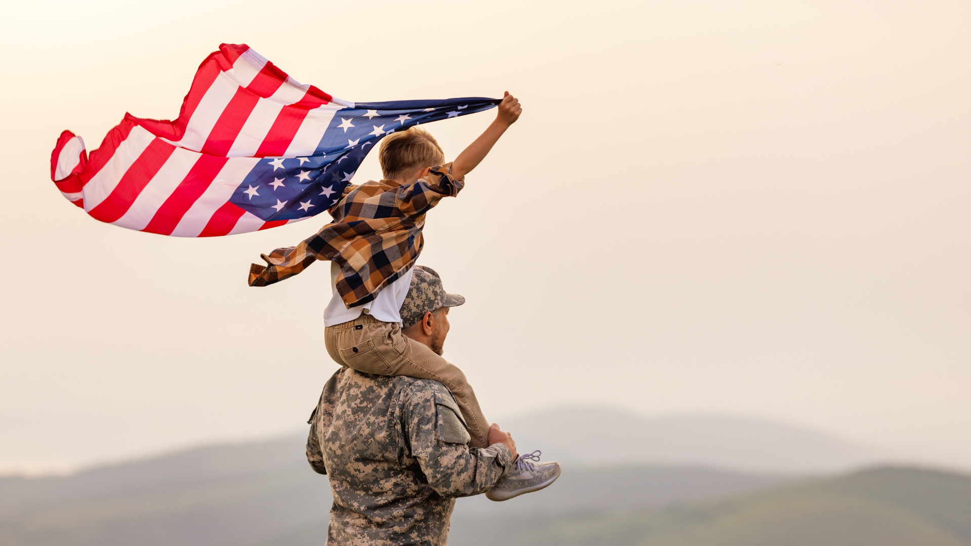 Soldier carrying a child holding an American flag at sunset