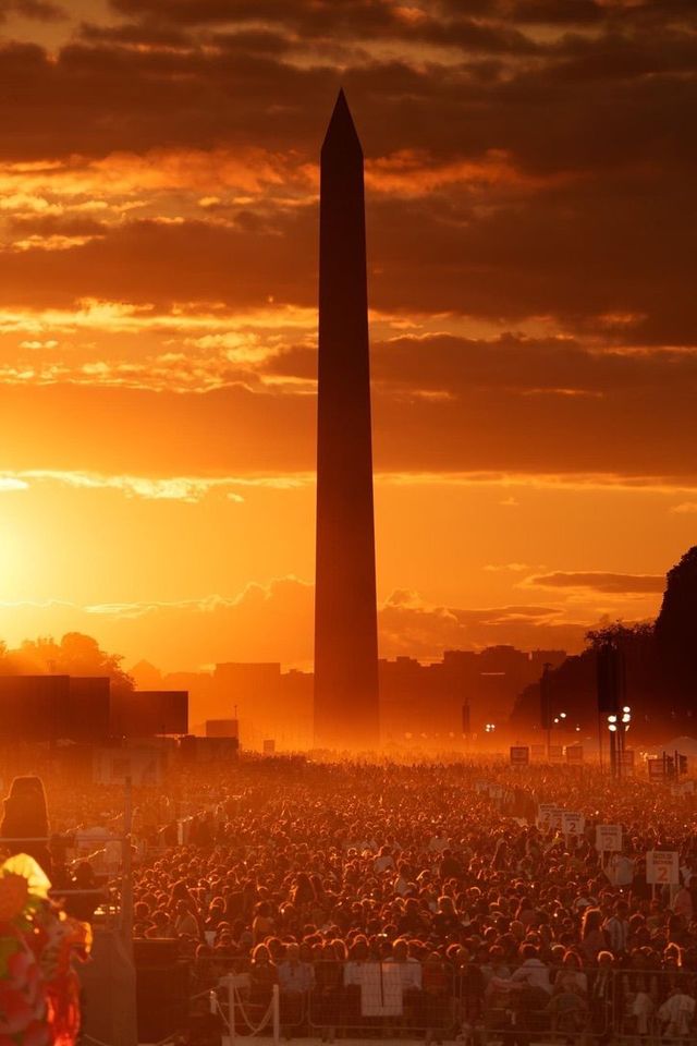 A large crowd is gathered in front of the washington monument at sunset