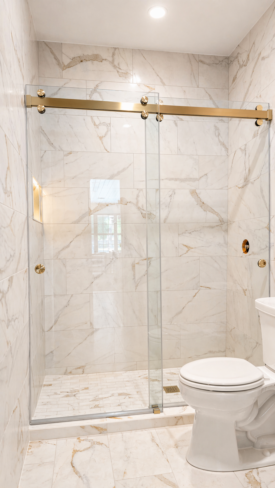 Modern bathroom shower with marble-look walls, glass door, gold hardware, and a white toilet.