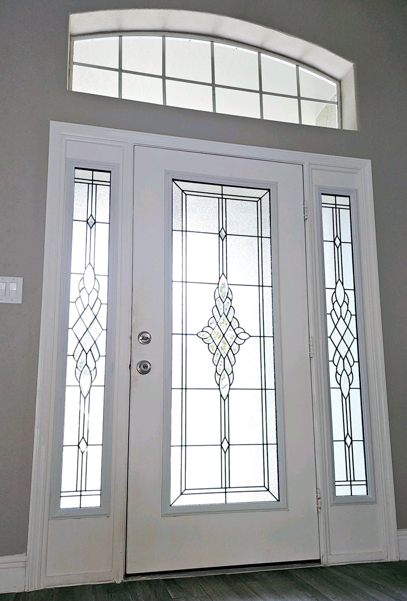 White front door with decorative glass panes and arched window above.