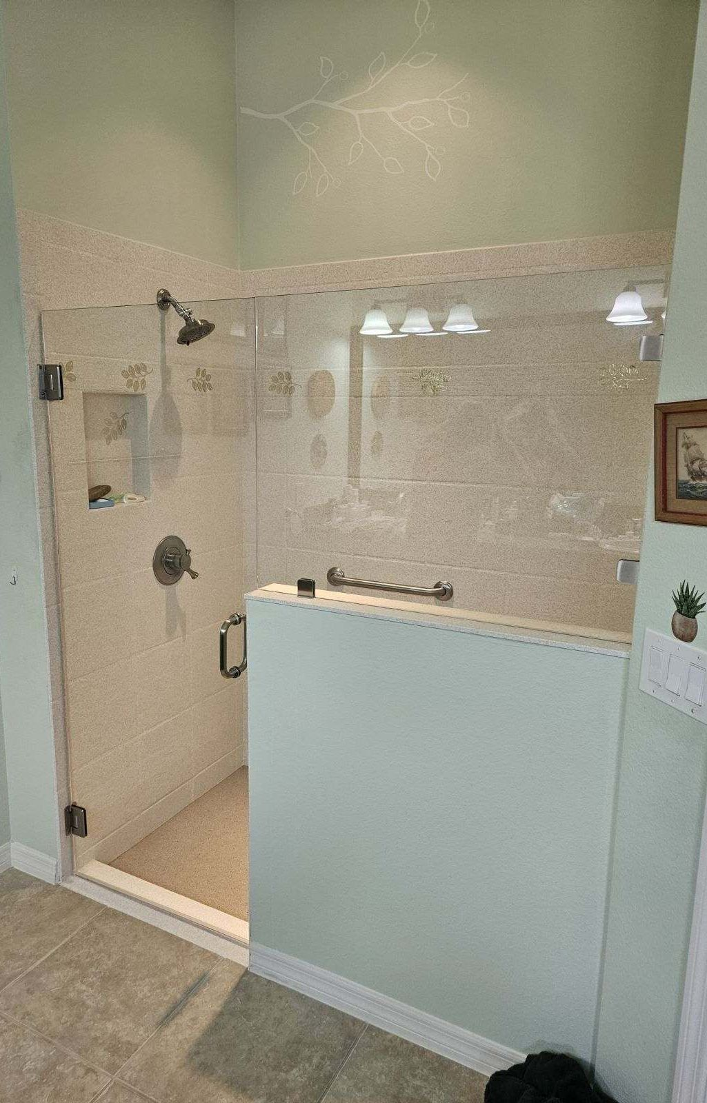A walk-in shower with clear glass doors and light-colored tile walls, set in a light-green bathroom.