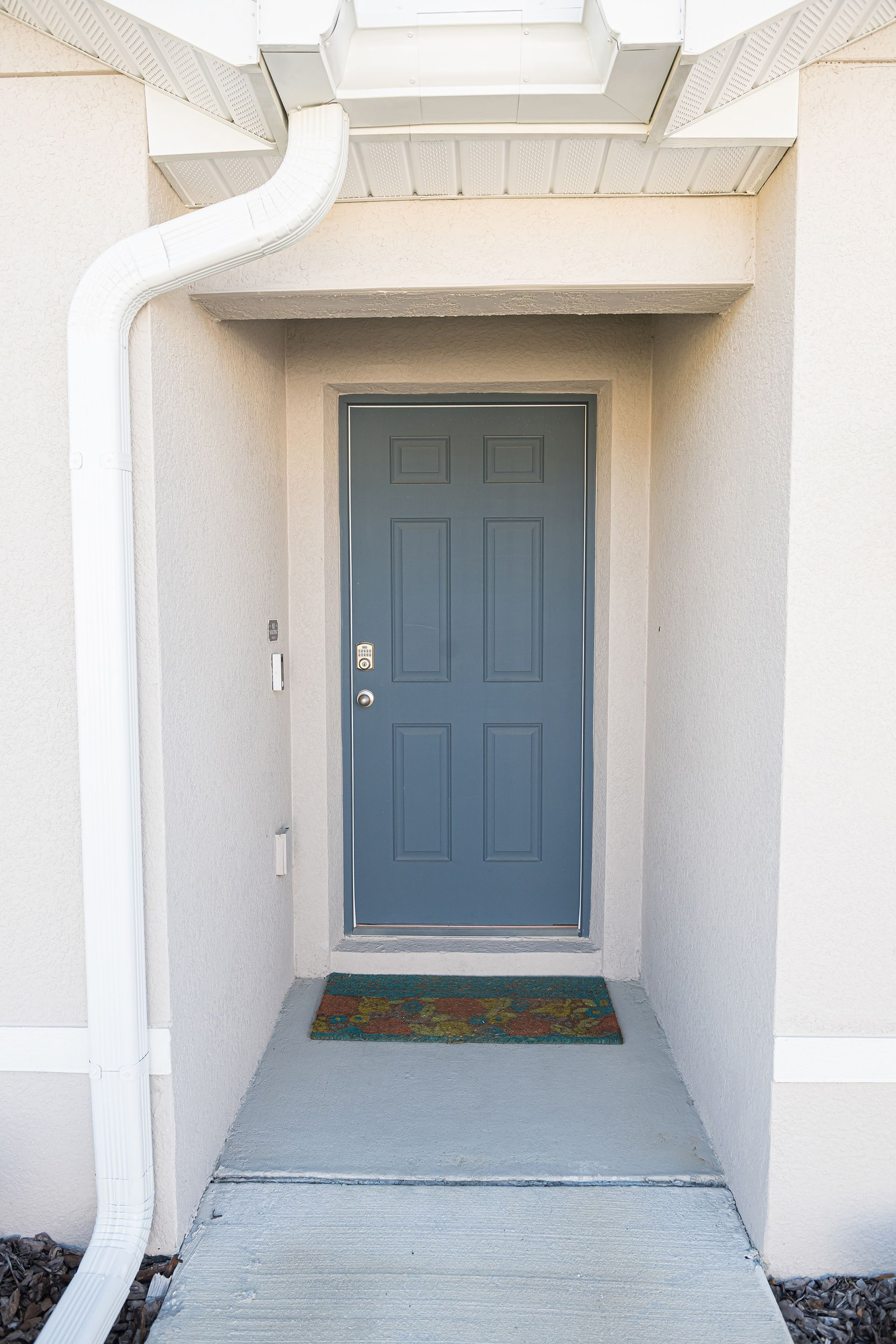 Blue front door within a recessed entryway, flanked by white walls and a white gutter.