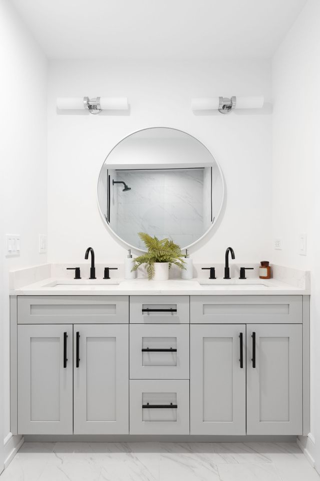 Modern bathroom with a light gray double vanity, round mirror, and black fixtures.