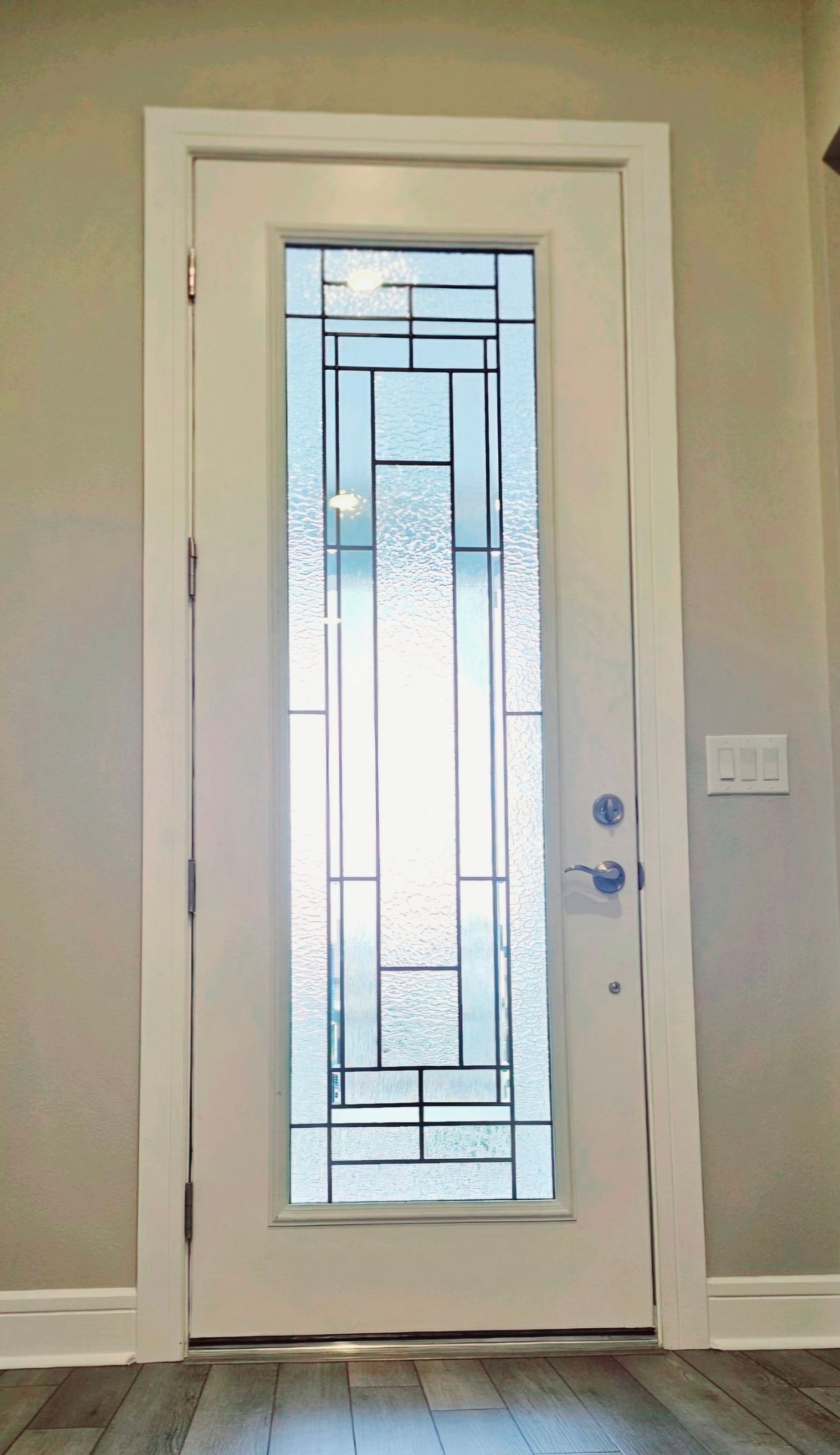 White front door with frosted glass panel and decorative geometric design, framed by light walls and tile floor