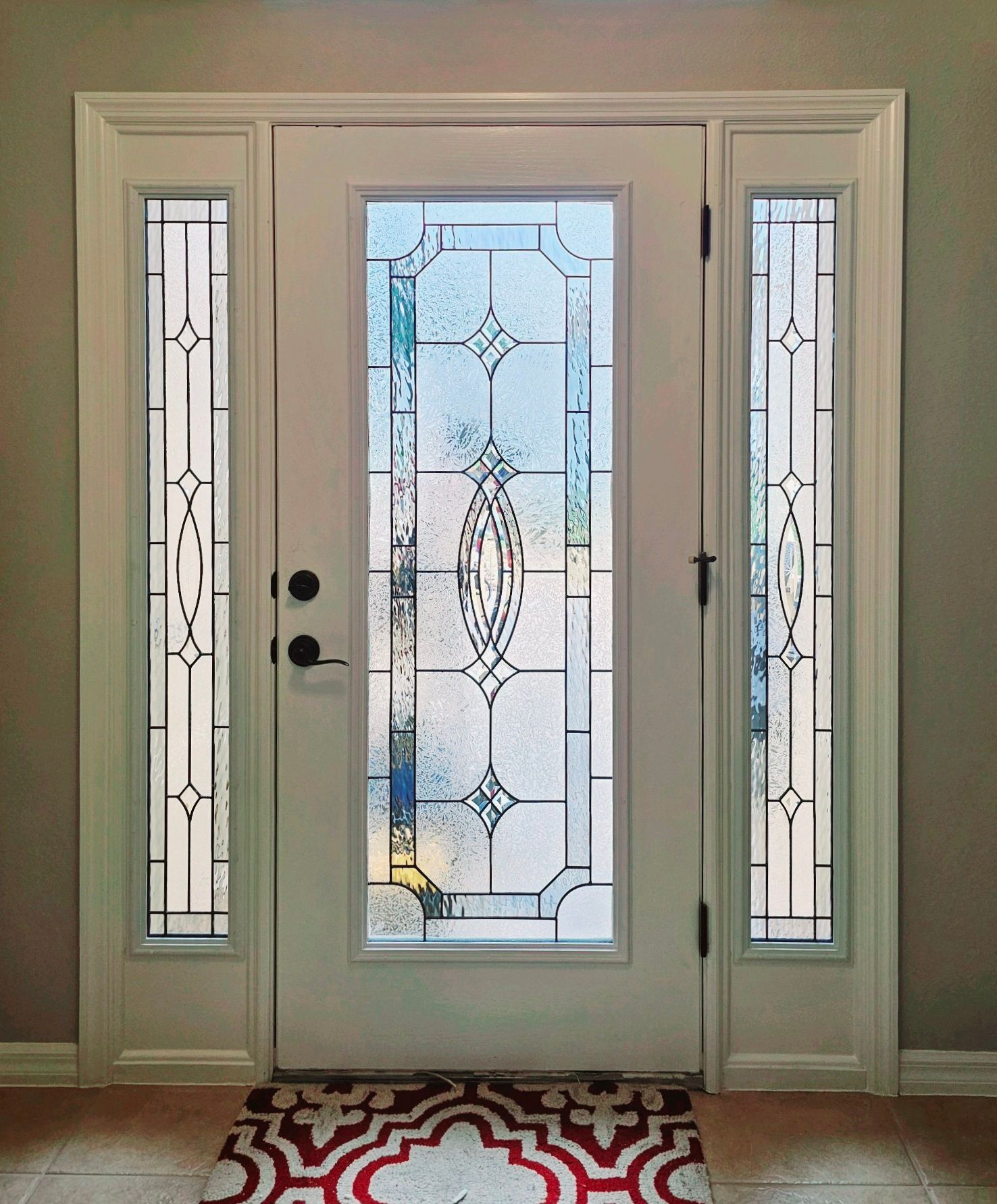 Front door with decorative frosted glass sidelights and a patterned red-and-white rug in front