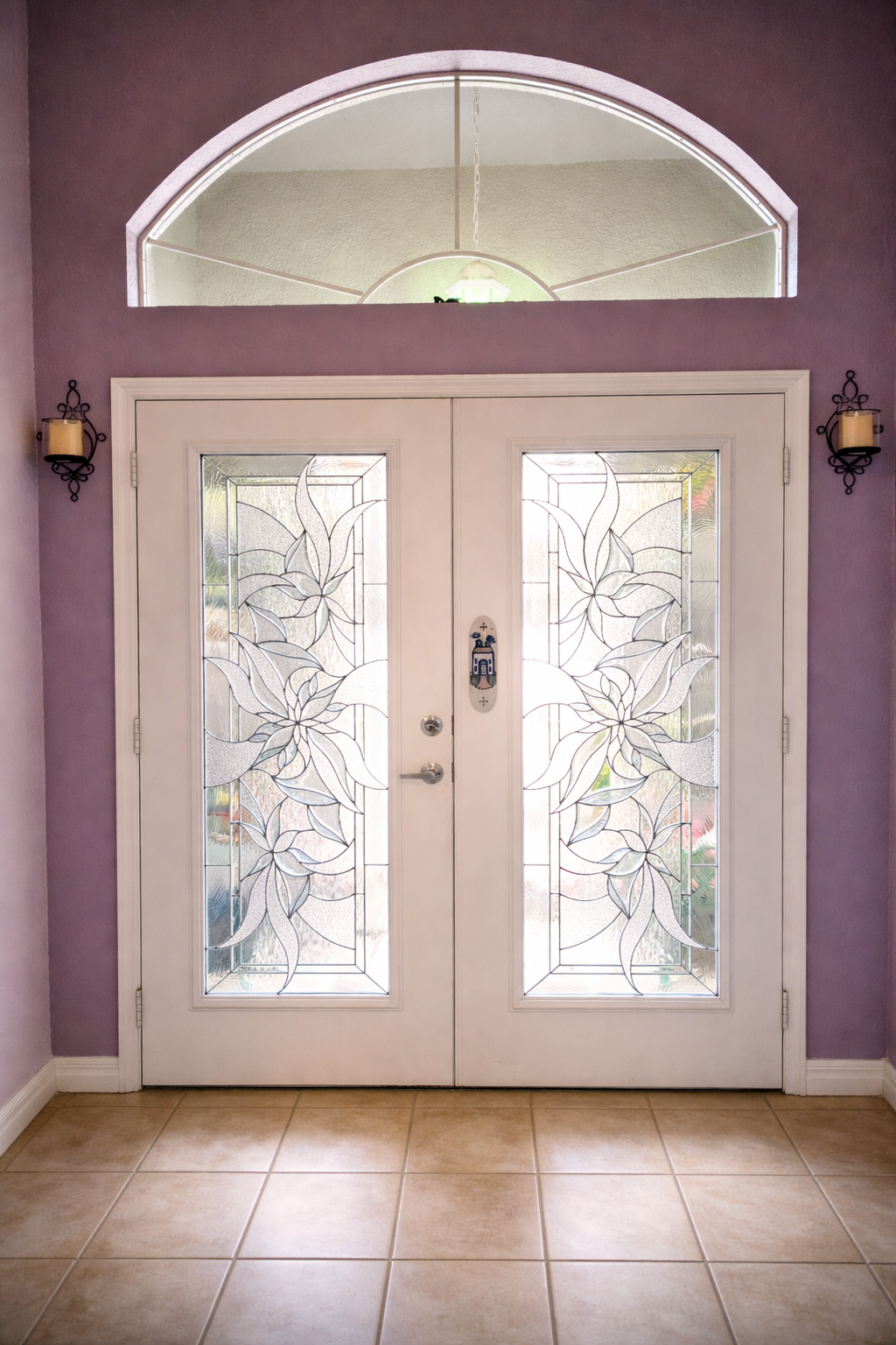 Front entry with double frosted glass doors, purple walls, tan tile floor, and arched transom window.