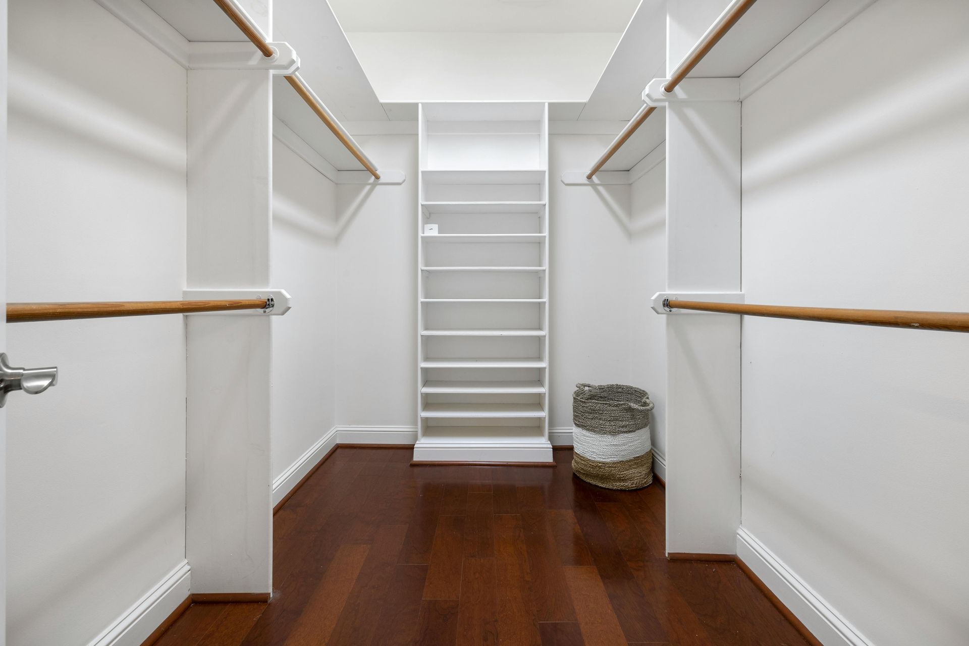 Empty walk-in closet with white shelves, hanging rods, and dark wood floors.