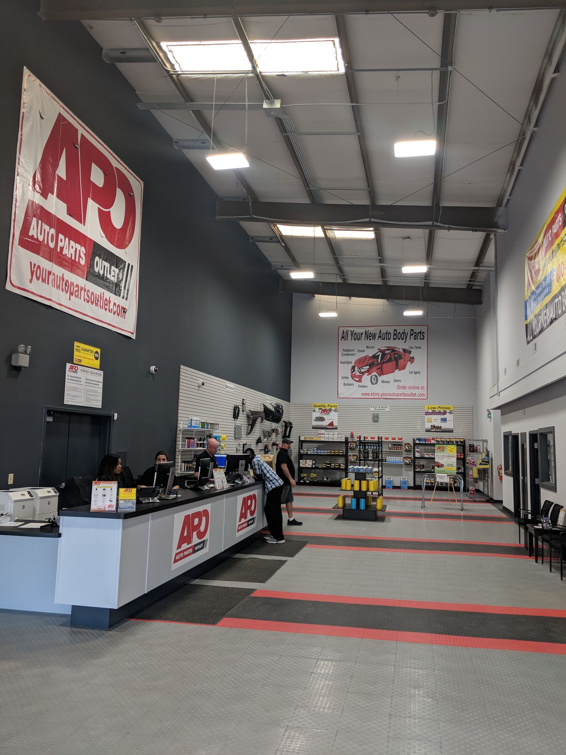 An auto parts store interior with a long service counter, concrete floors, high ceilings, and branding for APO.