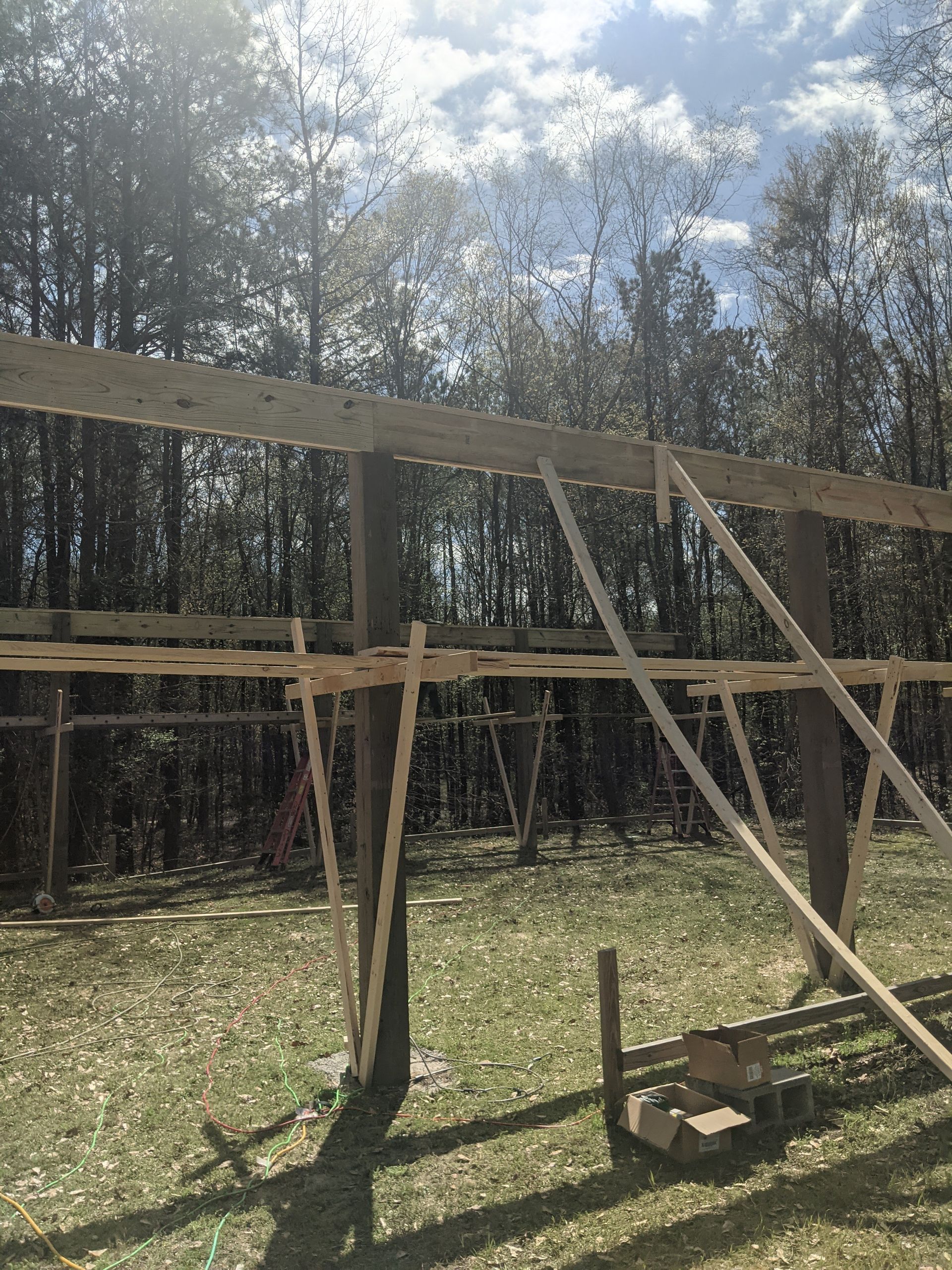 Wooden support beams stand upright in a field, reinforced by diagonal bracing and horizontal planks during construction.
